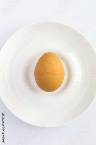 Ugly food. Ugly brown chicken egg on the white plate on the white background. Location vertical. Top view.