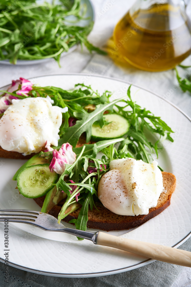 Poached eggs with herbs, avocado and cucumber served on a plate on a light background Copy space