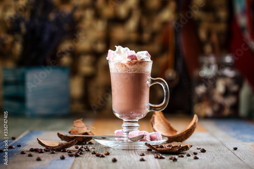 Side view tasty hot cocoa chocolate with whipped cream with marshmallows in a glass mug on a wooden background, horizontal