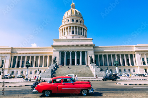 Brightly colored classic American cars serving as taxis pass on the main street in front of the Capitolio building in Central Havana, Cuba. © Curioso.Photography
