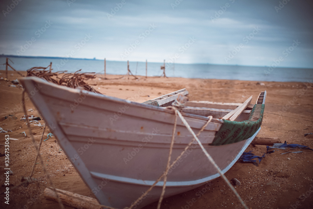 White blue traditional boat on sandy beach . Wooden boat on beach . Retro vintage toned fishing boat on the beach with blue sky and the sea on the background .