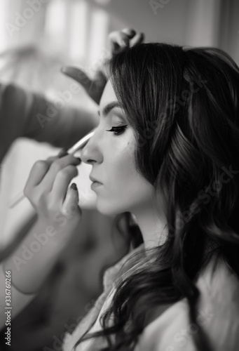 Young beautiful bride applying wedding make-up by make-up artist. Morning preparation. Close-up.