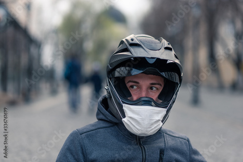 portrait of a man in a helmet. on a motorcycle helmet a white medical mask. photo on the street against the background of houses. coronavirus, disease, infection, quarantine, covid-19