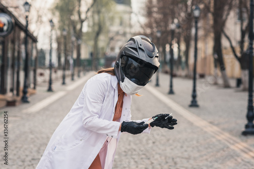 a thin girl in a white medical coat and overalls holds a syringe. A woman in a motorcycle helmet with a medical mask. coronavirus, disease, infection, quarantine, covid-19