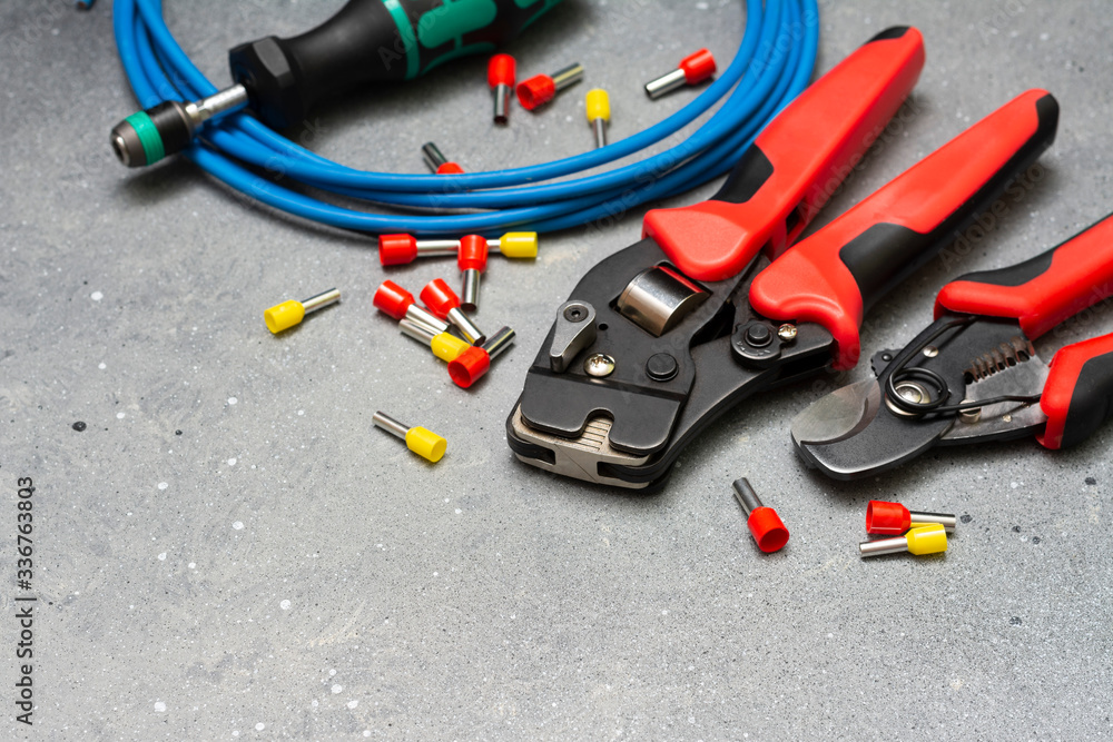 Tools and tips of different sizes and colors for crimping stranded electrical wires. Crimping tools, wire tips and electrical cable on a grey concrete background