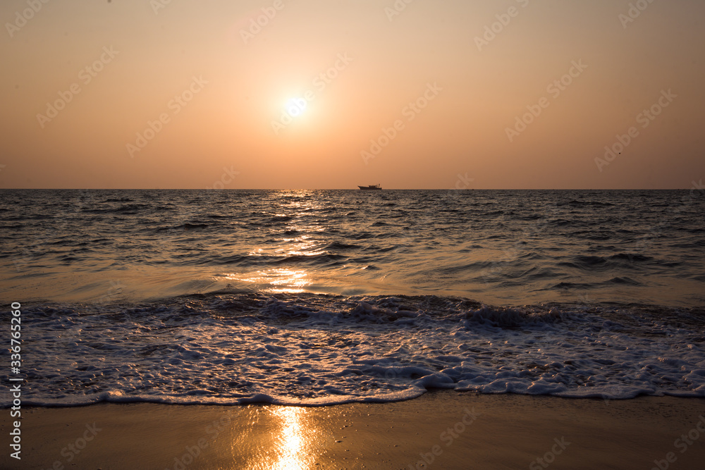 Orange sunset in the sea in India - orange and pink sky, dark blue sea. The outline of a ship on the horizon at sea