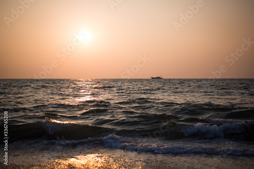 Orange sunset in the sea in India - orange and pink sky  dark blue sea. The outline of a ship on the horizon at sea