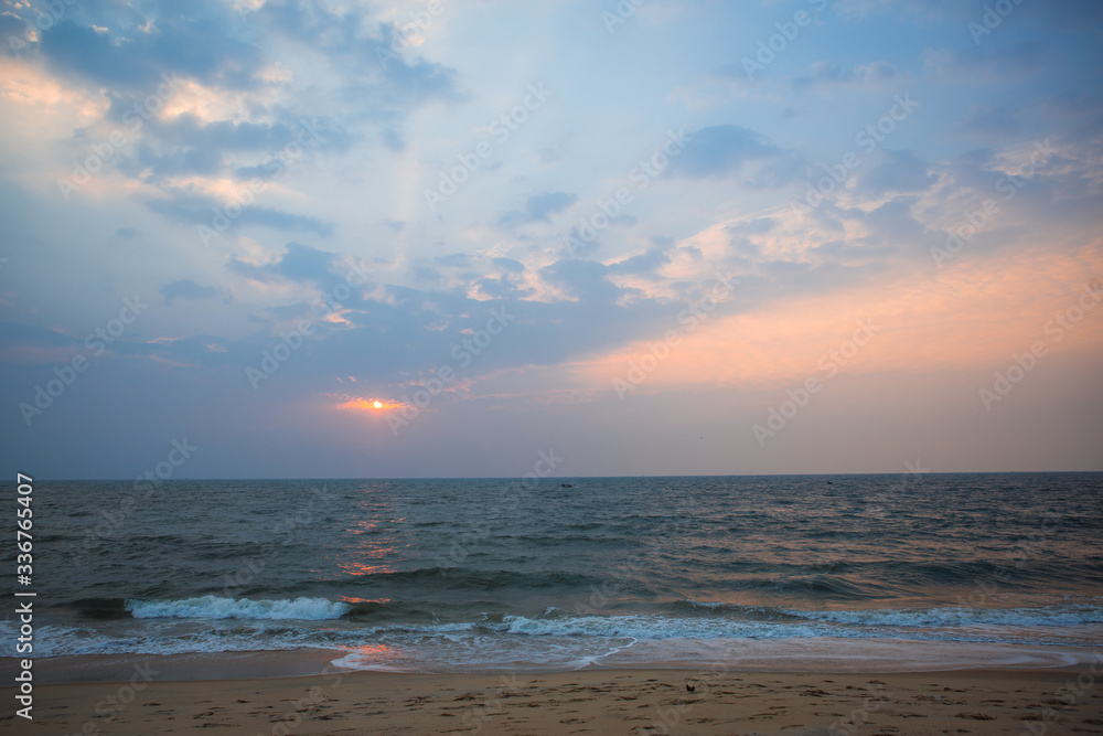 Orange sunset in the sea in India - orange and pink sky, dark blue sea. The outline of a ship on the horizon at sea