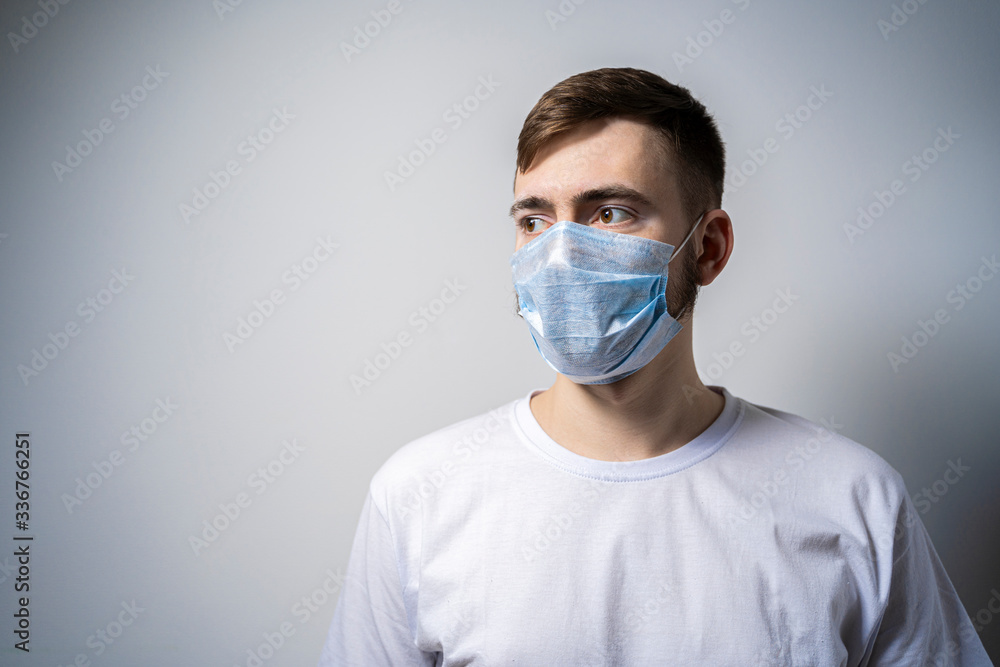 A young man in a medical mask on a white background looks away. Self isolation A young man in a medical mask on a white background looks away. Self isolation
