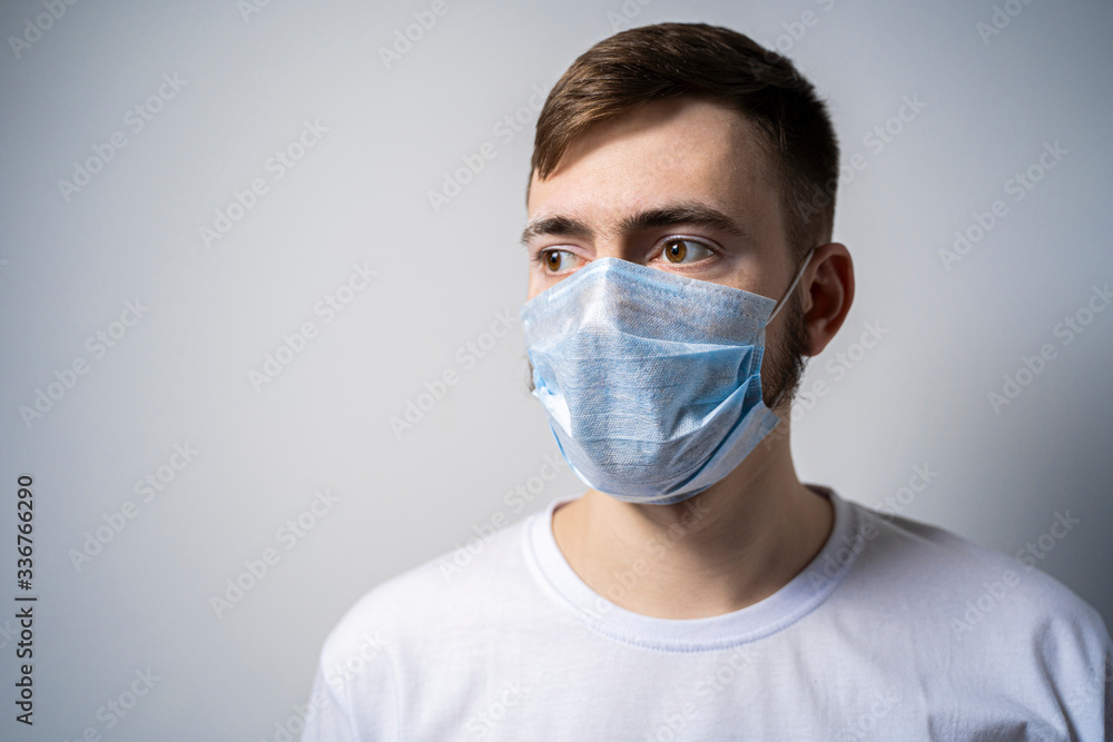 A young man in a medical mask on a white background looks away. Self isolation A young man in a medical mask on a white background looks away. Self isolation