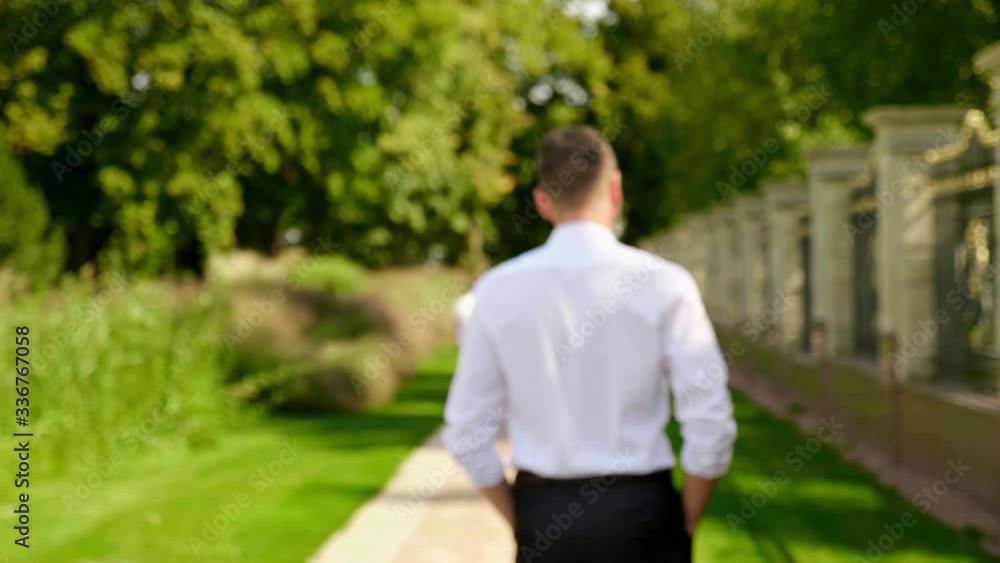 A businessman in a white shirt and trousers walks in the park. Defocus. 4K footage A businessman in a white shirt and trousers walks in the park. Defocus. 4K footage