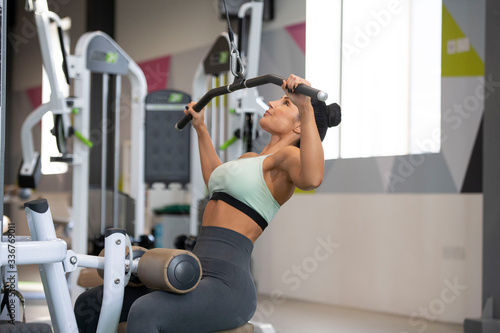 Beautiful caucasian brunette athletic girl on a lat pull down machine as she exercises in a gym or health club