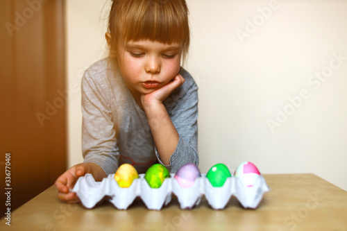 toddler girl looking at a paper tray with self decorated easter eggs