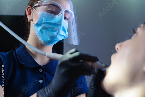 close-up, from an unusual angle, view, a dentist using dental equipment treats a patient a girl with a tooth and oral cavity disease. In the dental office.