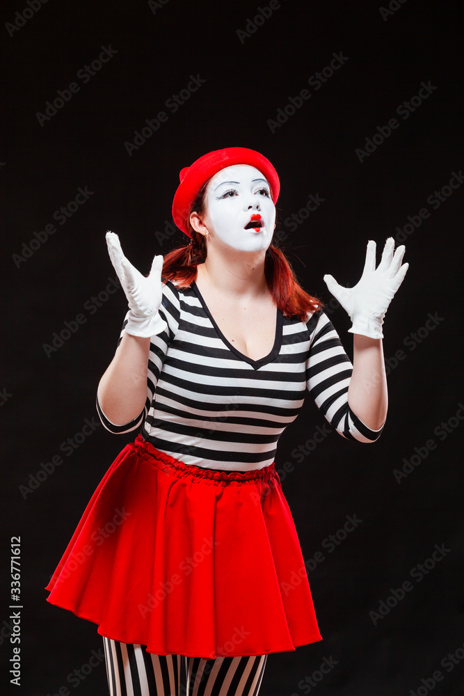 Portrait of female mime artist performing, isolated on black background. Woman in striped clothes and red skirt is standing with raised hands amazed. Symbol of wonder, admiration, worship Portrait of female mime artist performing, isolated on black background. Woman in striped clothes and red skirt is standing with raised hands amazed. Symbol of wonder, admiration, worship