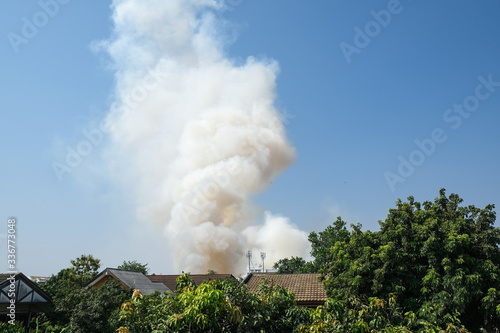 fire on grass with white smoke overview in city blowing on blue sky. emergency danger air pollution in summer season.