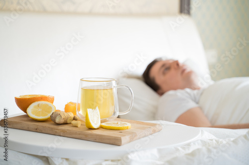 Cup with antipyretic drugs for colds,flu.Sick man in bed. Tea with citrus vitamin C,ginger root,lemon,orange.Wooden tray. Home self-treatment.Medical quarantine antiviral covid-19 coronavirus therapy