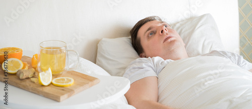 Cup with antipyretic drugs for colds,flu.Sick man in bed. Tea with citrus vitamin C,ginger root,lemon,orange.Wooden tray. Home self-treatment.Medical quarantine antiviral covid-19 coronavirus therapy