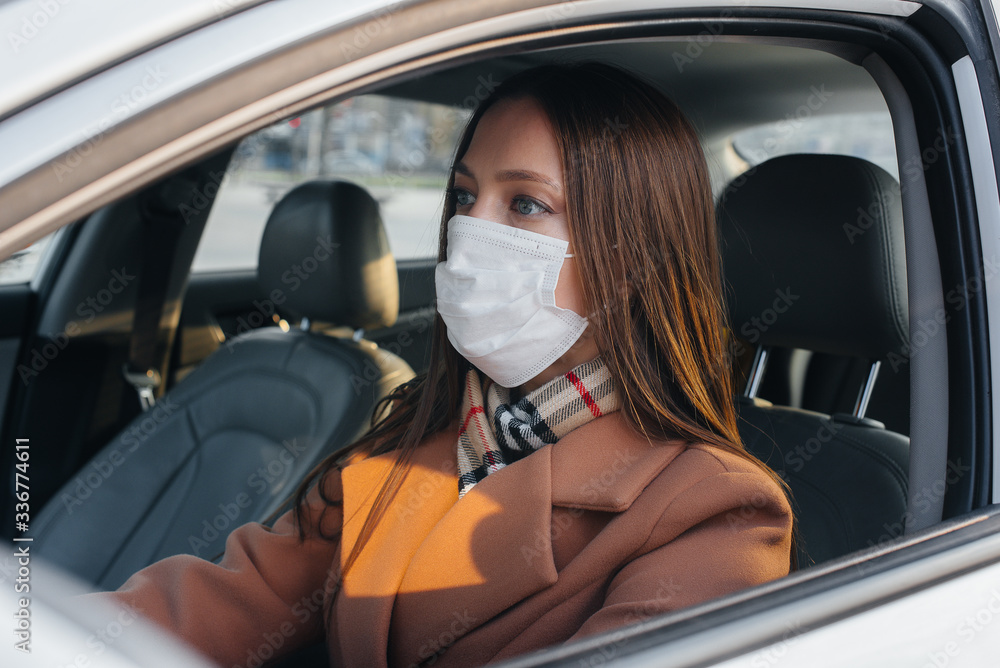 A young girl sits behind the wheel in the car in the mask during the global pandemic and coronavirus. Quarantine A young girl sits behind the wheel in the car in the mask during the global pandemic and coronavirus. Quarantine