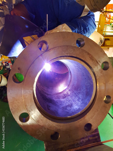 Close up view of welder welding a pipe with flange