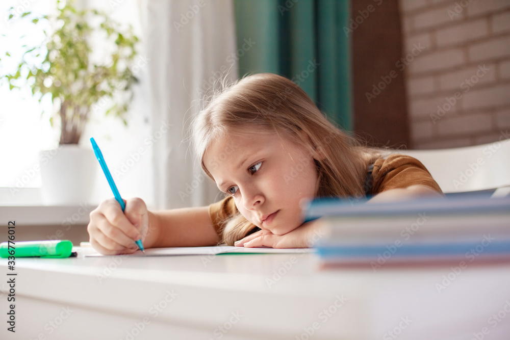 A beautiful girl writes with a pen in a notebook. The child performs homework. Home training, online training A beautiful girl writes with a pen in a notebook. The child performs homework. Home training, online training