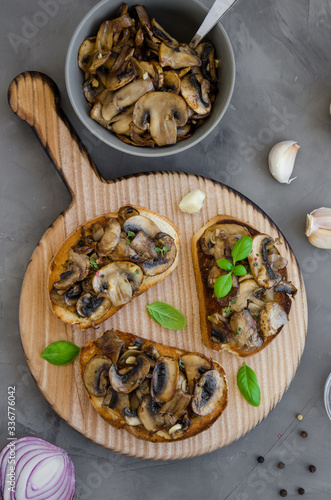 Bruschetta with fried mushrooms with onion, garlic, thyme and basil on a cutting board on a dark concrete background. Vertical orientation. Top view.