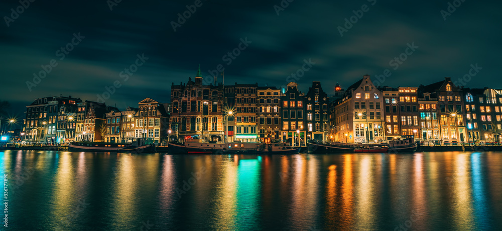 Amsterdam City panorama, illuminated buildings or dancing houses with reflection in water canal at night, Netherlands.