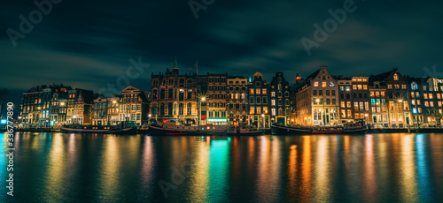 Amsterdam City panorama, illuminated buildings or dancing houses with reflection in water canal at night, Netherlands.