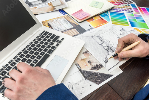 Architects hands drawing of modern apartaments with colour sample and laptop on creative desk, office. Man choosing colors for room decoration.