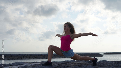 attractive girl doing yoga by the ocean, warrior pose