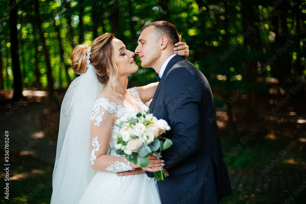 The bride and groom walk together in the park. Charming bride in a white dress, the groom is dressed in a dark elegant suit. The bride and groom walk together in the park. Charming bride in a white dress, the groom is dressed in a dark elegant suit.