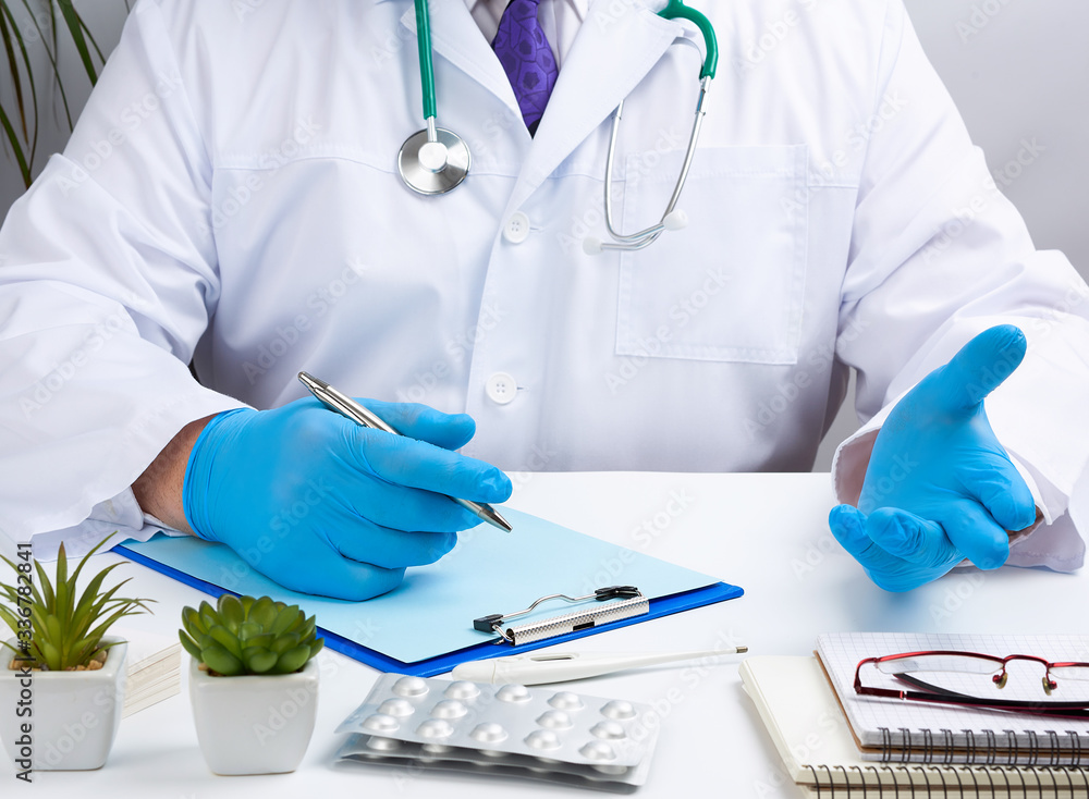 doctor in a white uniform sits at a white table and writes in a paper notebook, wearing sterile gloves on his hands doctor in a white uniform sits at a white table and writes in a paper notebook, wearing sterile gloves on his hands