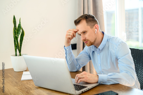 Guy in a formal shirt with airpods uses a laptop