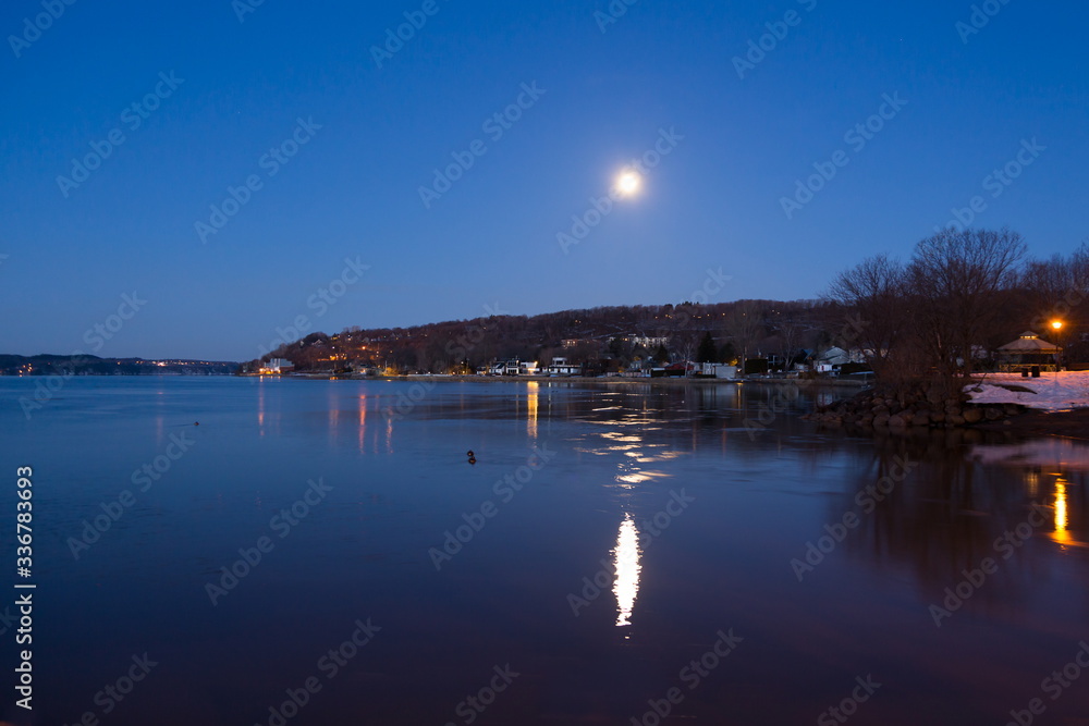 Fototapeta premium Bright full moon reflected in a St. Lawrence River cove during a blue hour dawn, Cap-Rouge area, Quebec City, Quebec, Canada 
