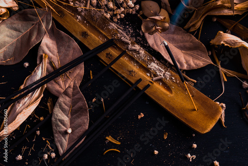 Stick holder and incense stick with leaves and flowers on black background