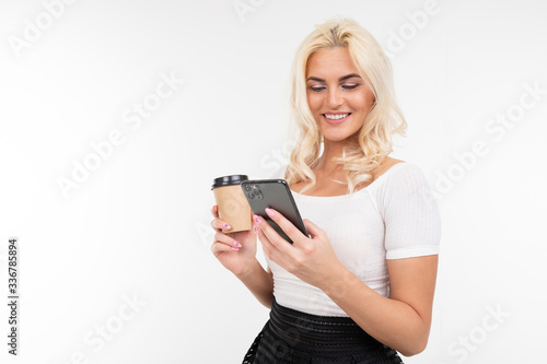lady in a white T-shirt on a break surfs in the phone and drinks coffee on a white background with copy space