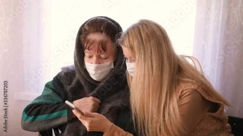 A young girl trains an elderly grandmother in a mask to use a mobile phone during the quarantine period of the coronavirus pandemic