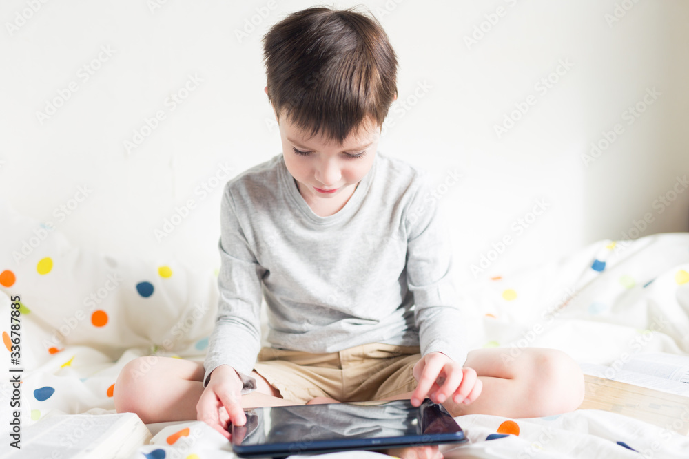 Game. Boy plays with smartphone. School Boy on bed at home with digital pad tablet in hand, doing homework. Distance learning online education. Quarantine. Game. Boy plays with smartphone Game. Boy plays with smartphone. School Boy on bed at home with digital pad tablet in hand, doing homework. Distance learning online education. Quarantine. Game. Boy plays with smartphone