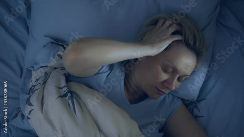 a woman suffering from insomnia lies in bed in the dark with her eyes open.