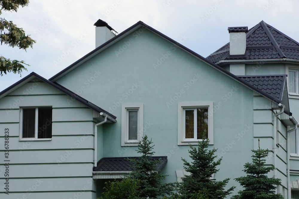 facade of a large private house with a green wall and white windows under a tiled roof and chimneys against a gray sky facade of a large private house with a green wall and white windows under a tiled roof and chimneys against a gray sky