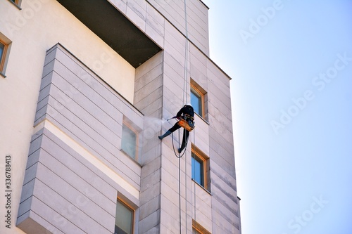 Rope access facade maintenance. Worker cleaning a stone exterior of apartment building facade. photo