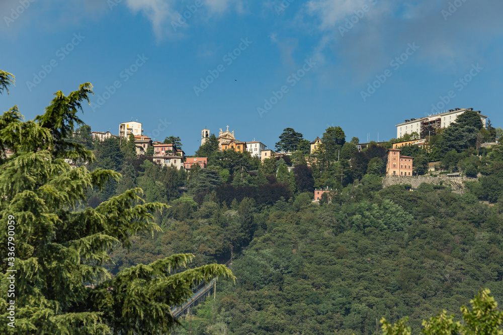 Como, ITALY - August 4, 2019: Apartments, villas, hotels on the green forested mountainsides near Lake Como. Beautiful Italian Como city. Warm sunny summer day in very popular holiday destination