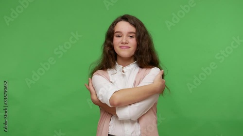 I am beautiful, love myself! Dreamy attractive young brunette girl in white shirt embracing herself and smiling from pleasure, teenage complacency. indoor studio shot isolated on green background