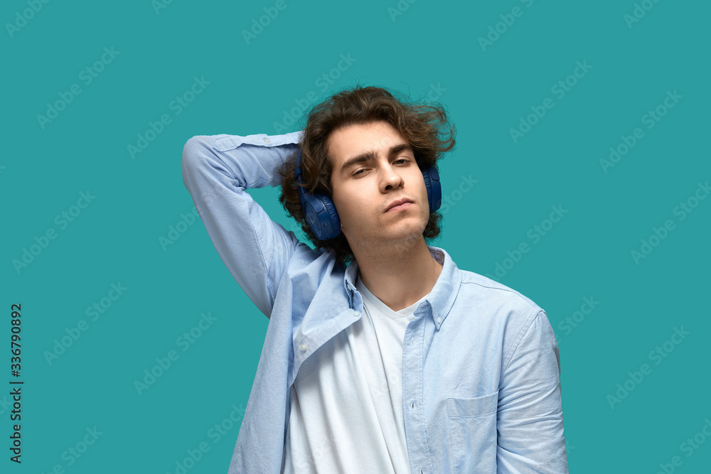 Portrait of a young beautiful man wearing white t-shirt and blue shirt in headphones over blue background