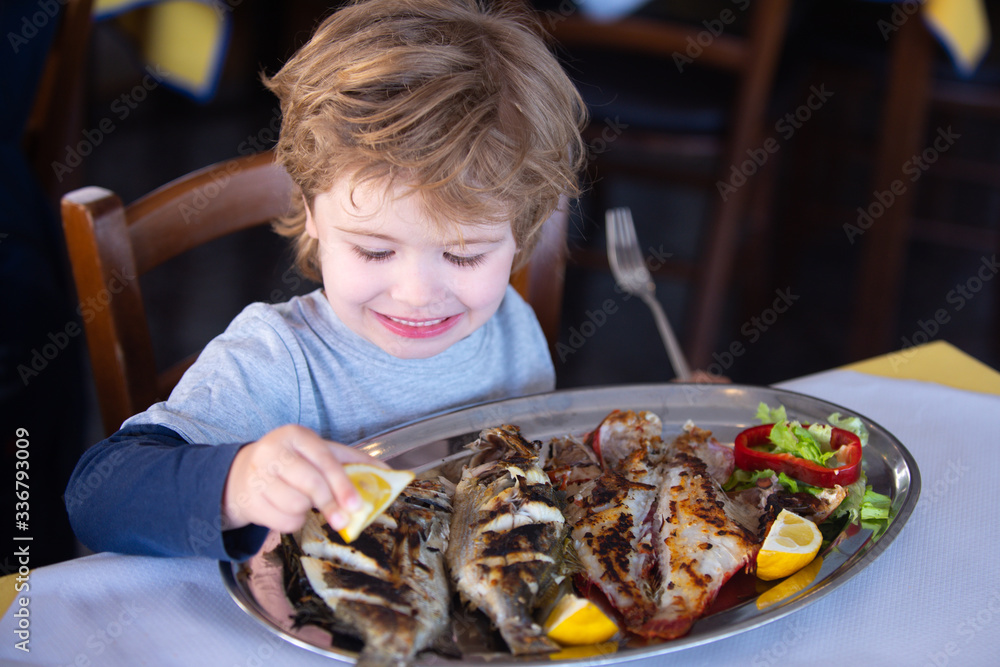 Lemon for fish. Boy pours lemon juice on fish in restaurant. Lunch at ...