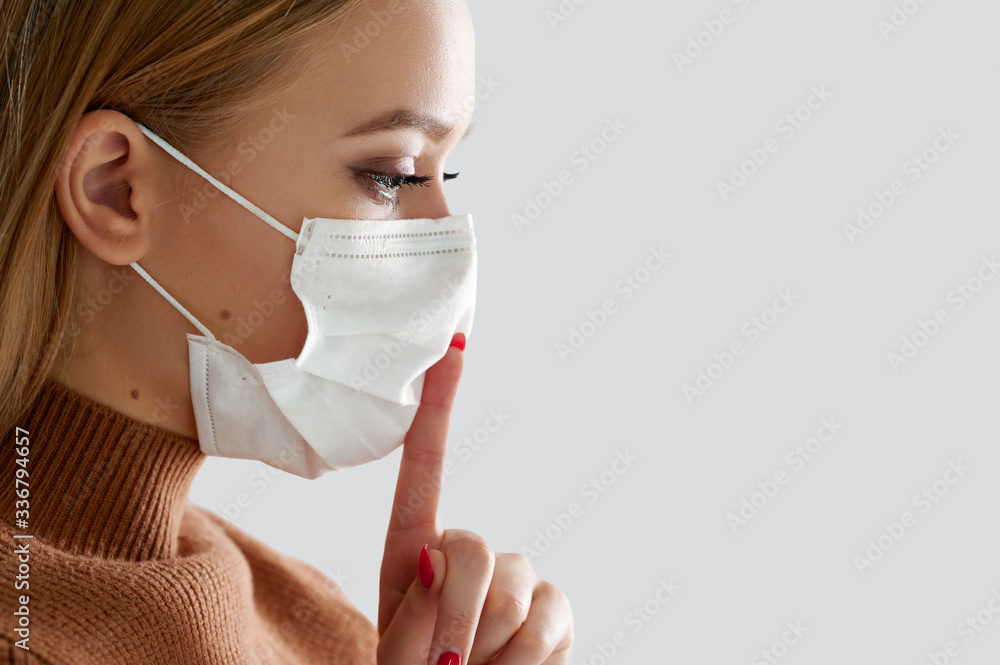 Close portrait woman in medical protective mask holds finger near lips Close portrait woman in medical protective mask holds finger near lips