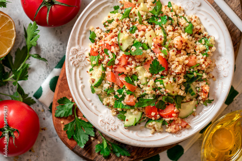 Tabbouleh salad - traditional Middle Eastern or Arabic cuisine. Levantine vegetarian salad with bulgur, quinoa, tomato, cucumber, parsley and lemon juice. Tabbouleh with bulgur top view.