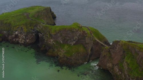 4k aerial video of a rope bridge crossing onto an island surrounded by beautiful water and green grass