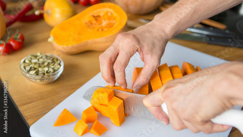Man hands slicing pumpkin on cubes on cutting board