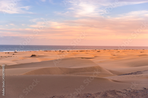 People passing through sand dunes overlooking the ocean on the horizon during a sunny day with thick clouds moving in the sky from the Grand Canary Island